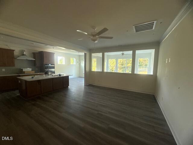 Spacious open-plan room with dark wood floors, a kitchen area with island and cabinets on the left, and a bright sunroom with large windows at the back. Ceiling fans and recessed lighting are visible.