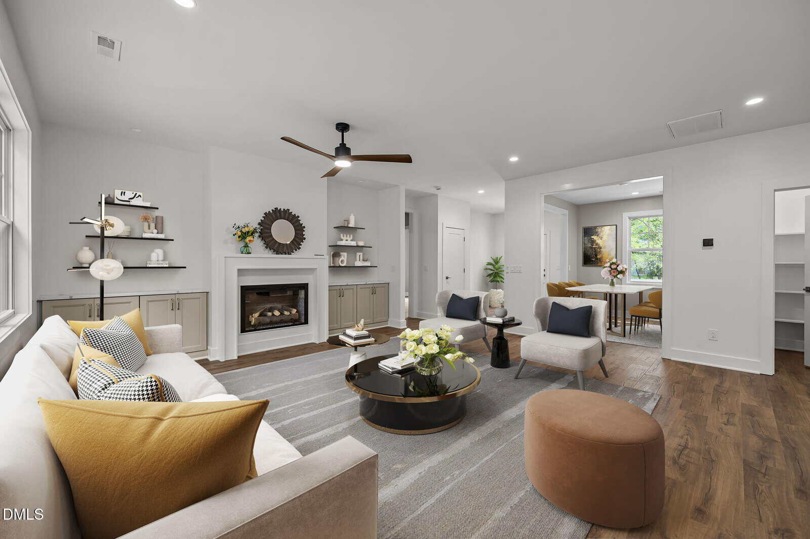 Modern living room with neutral tones, a tan sofa with yellow pillows, round coffee tables, armchairs, a fireplace with a mirror above, shelves, wood floors, and a dining area visible in the background.