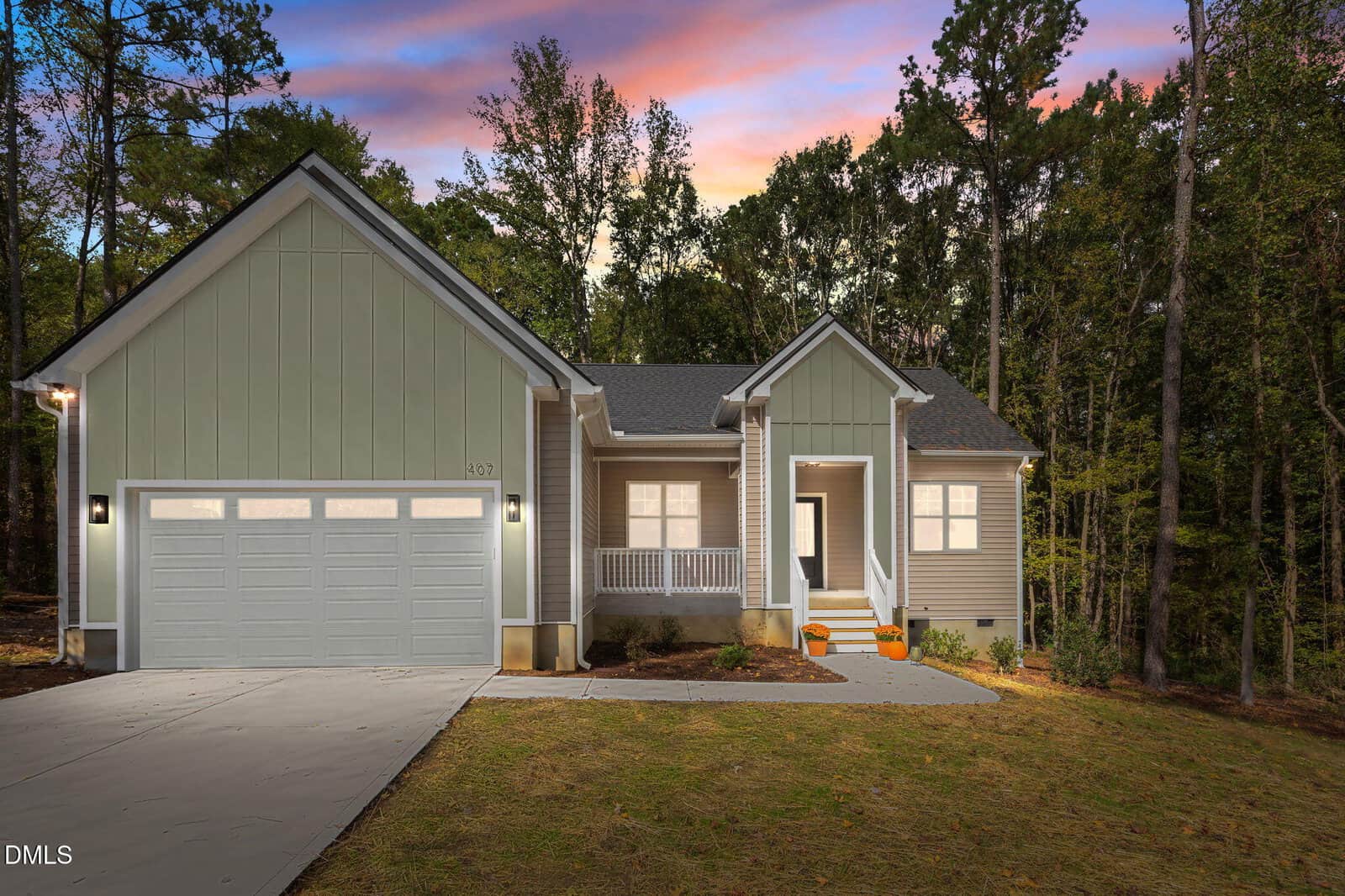 A modern, light gray single-story house at 407 Watson Street in Creedmoor features a double garage, white trim, and a front porch. Surrounded by trees at dusk with a colorful sky, two orange pumpkins sit by the front steps.