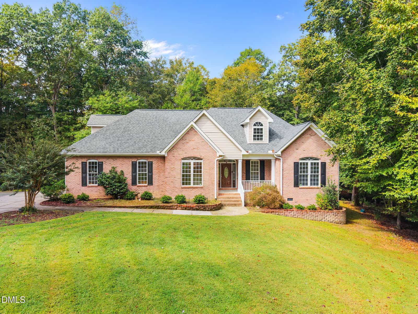 Single-story brick house at 1080 Wild Briar Lane in Stem with a gray roof, white trim, arched window above the entrance, and a neatly landscaped front yard bordered by trees under a clear blue sky.