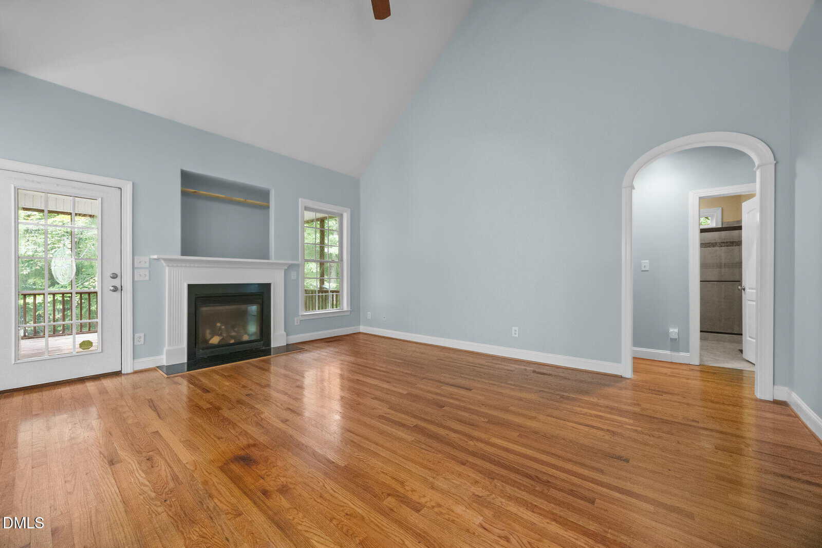 Spacious living room with hardwood floors, light blue walls, a fireplace, large windows, and a glass door leading to a screened porch. An arched doorway leads to another room.