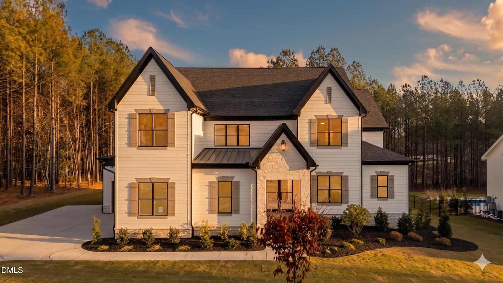 Modern two-story white house with black trim and roof at 190 Cherry Bark Drive, Youngsville, featuring large windows, stone accents around the front door, a landscaped yard, and trees under a partly cloudy sunset sky.