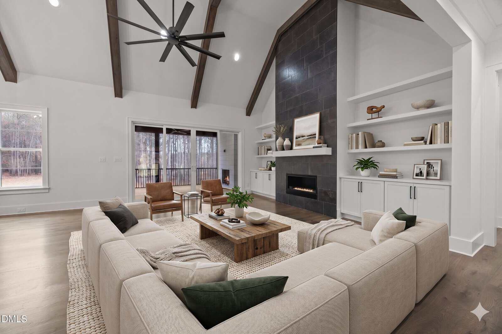 A modern living room with a beige sectional sofa, wooden coffee table, fireplace, built-in shelves, vaulted ceiling with wood beams, large windows, and neutral decor.