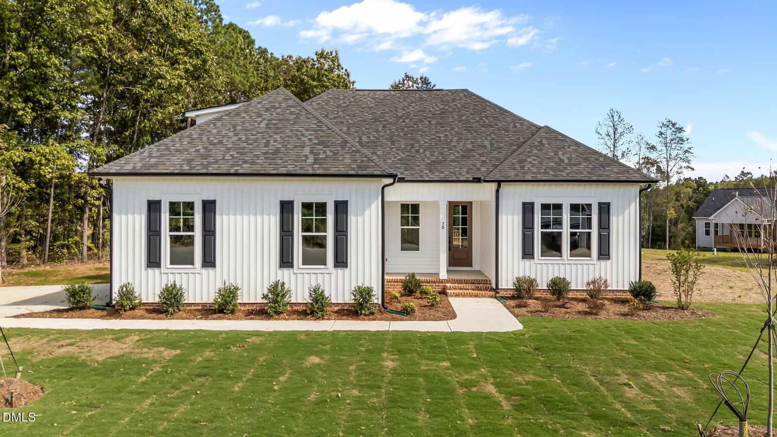Charming single-story white house at 70 Livingston Lane in Zebulon, featuring a dark gray roof, black shutters, and brick steps leading to a covered front porch. Fresh landscaping and a green lawn complete this inviting home.