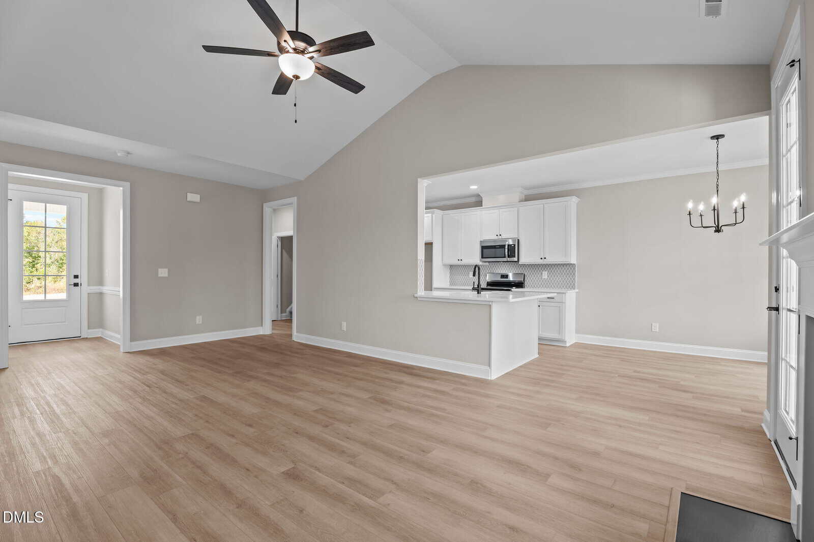 Open concept living area with wood floors, vaulted ceiling with ceiling fan, and large windows. Kitchen features white cabinets, stainless appliances, and a breakfast bar. Dining area includes a modern black chandelier.
