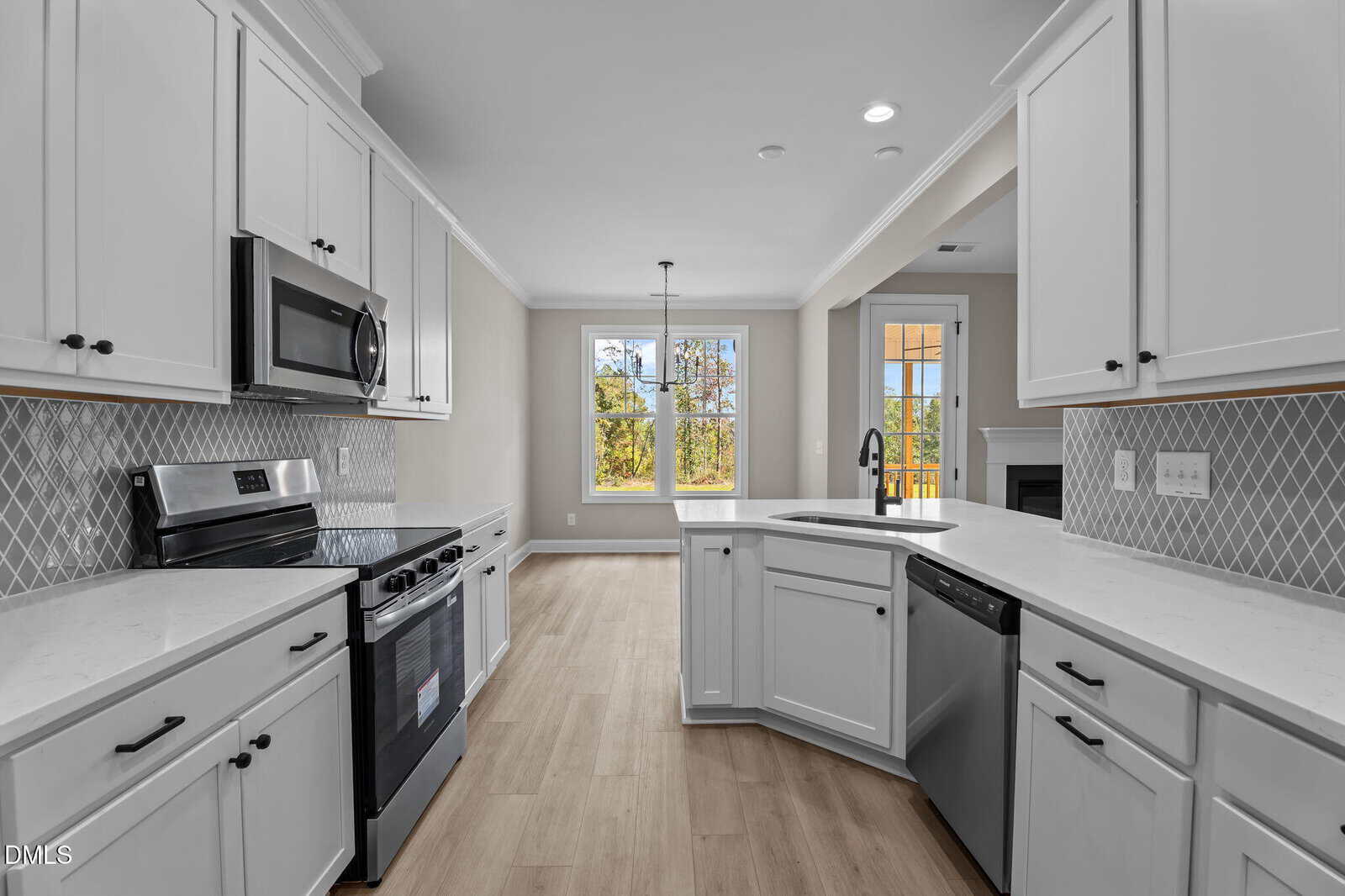 Modern kitchen with white cabinets, stainless steel appliances, gray patterned backsplash, and light wood flooring. Large windows and a glass door provide natural light, and an open layout connects to another room.