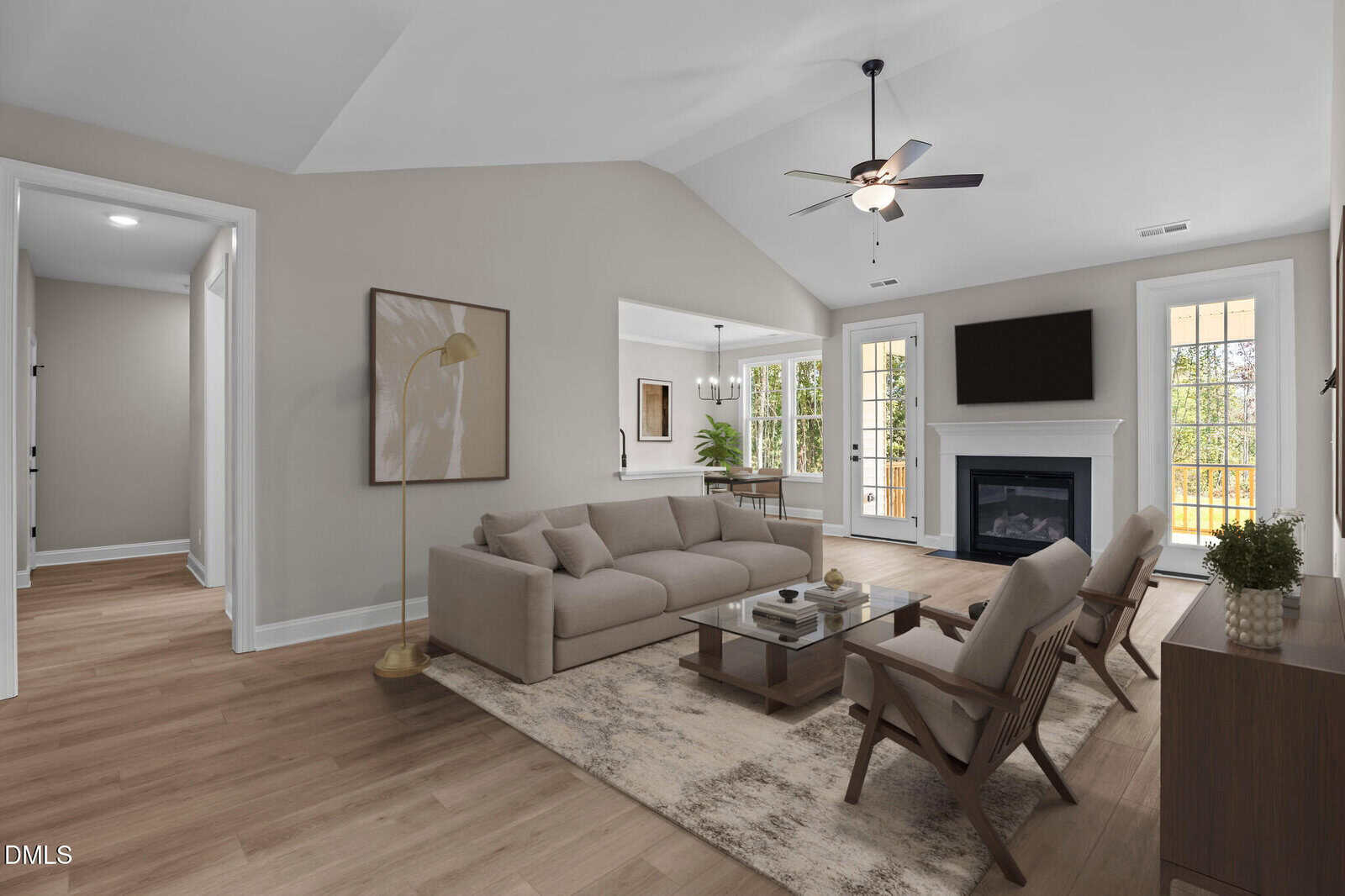 A modern living room with beige walls, light wood flooring, a sofa, two armchairs, a coffee table, a floor lamp, a fireplace with a TV above, and large windows letting in natural light.