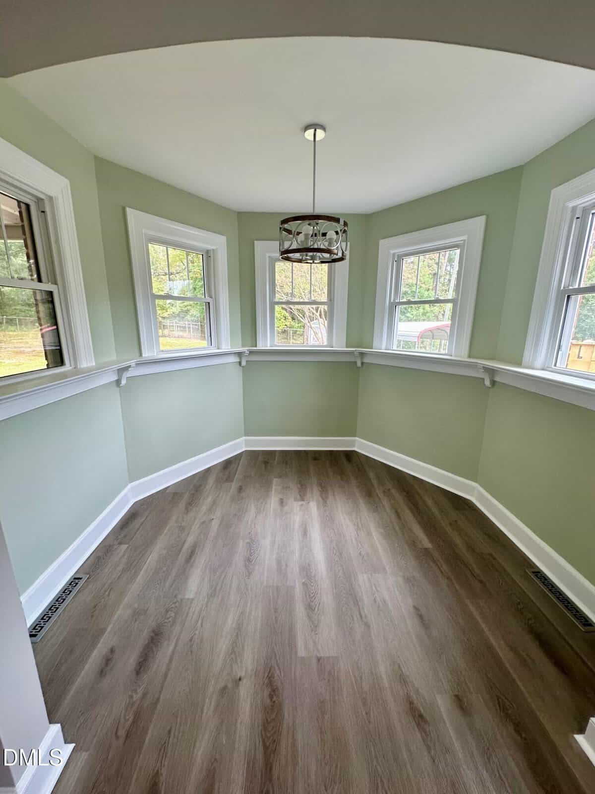 A small, octagonal room with pale green walls, white trim, five windows, wood-look flooring, a modern pendant light, and a narrow white ledge around the perimeter.