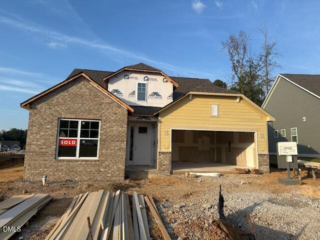 A single-family house under construction at 25 Bald Cypress Lane in Youngsville features a brick and yellow exterior, a two-car garage, and a โSoldโ sign in the window. Building materials and gravel are scattered on the ground in front.