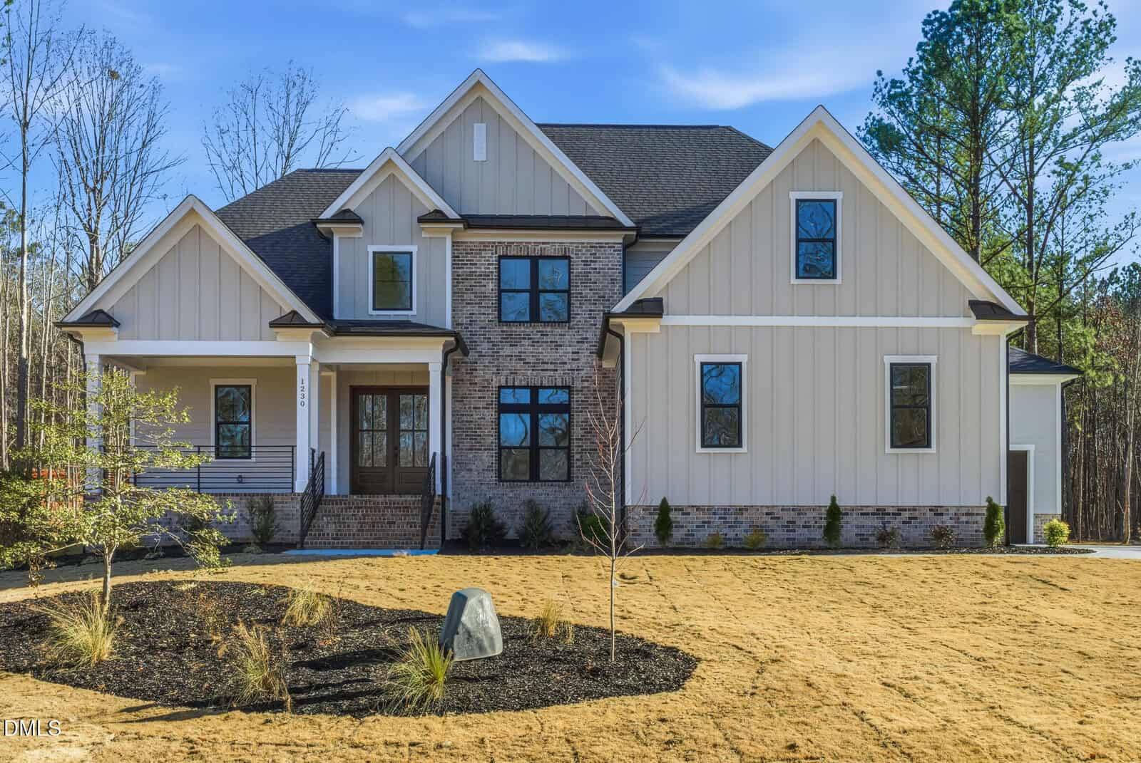 This two-story Youngsville home at 1230 Red Cedar Court features light-colored siding, brick accents, black-framed windows, and a small front porch. Fresh landscaping with mulch, small plants, and a patchy lawn complete the curb appeal.