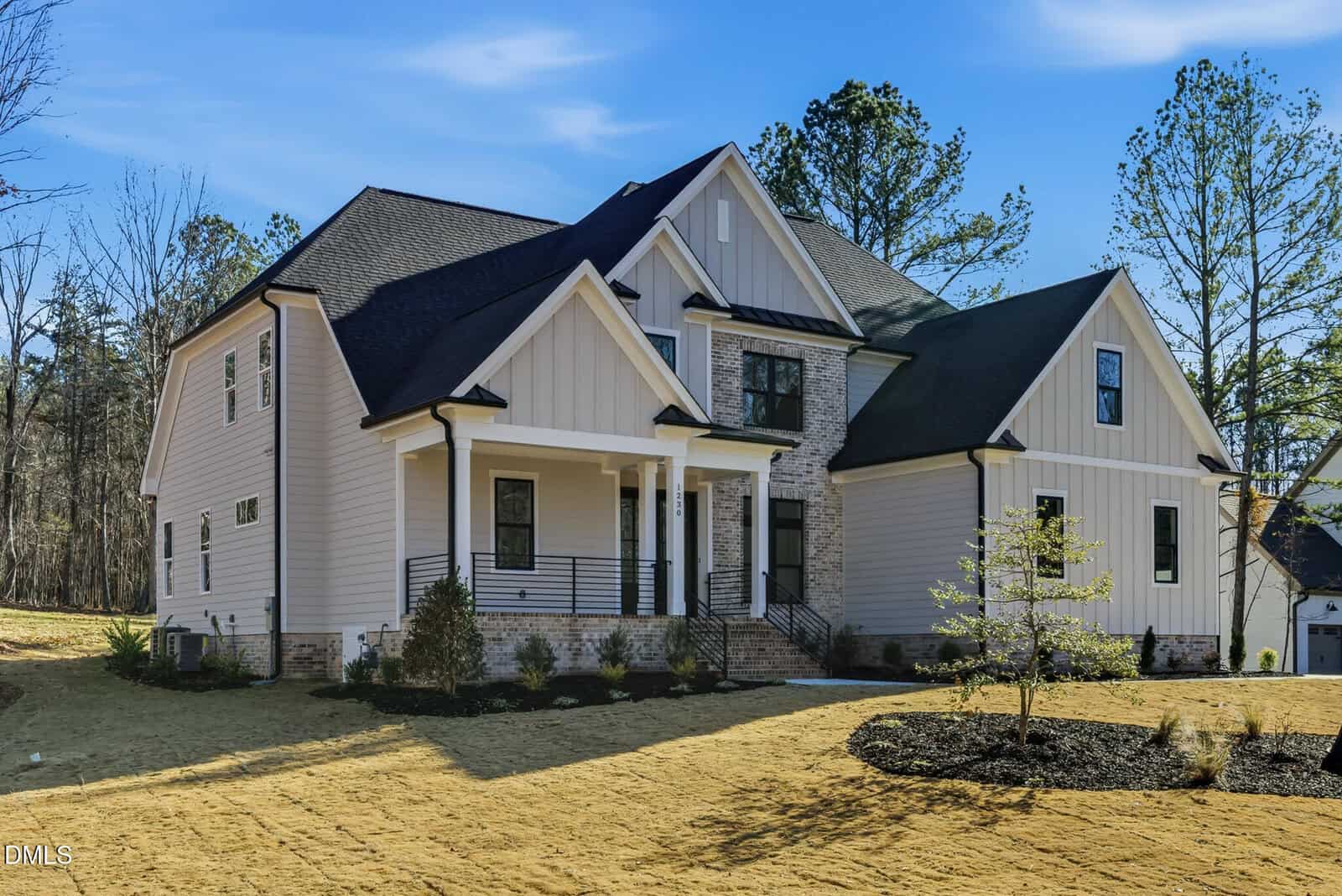 A two-story modern suburban house with white siding, dark gray roof, front porch, and landscaped yard, surrounded by trees and a clear blue sky.