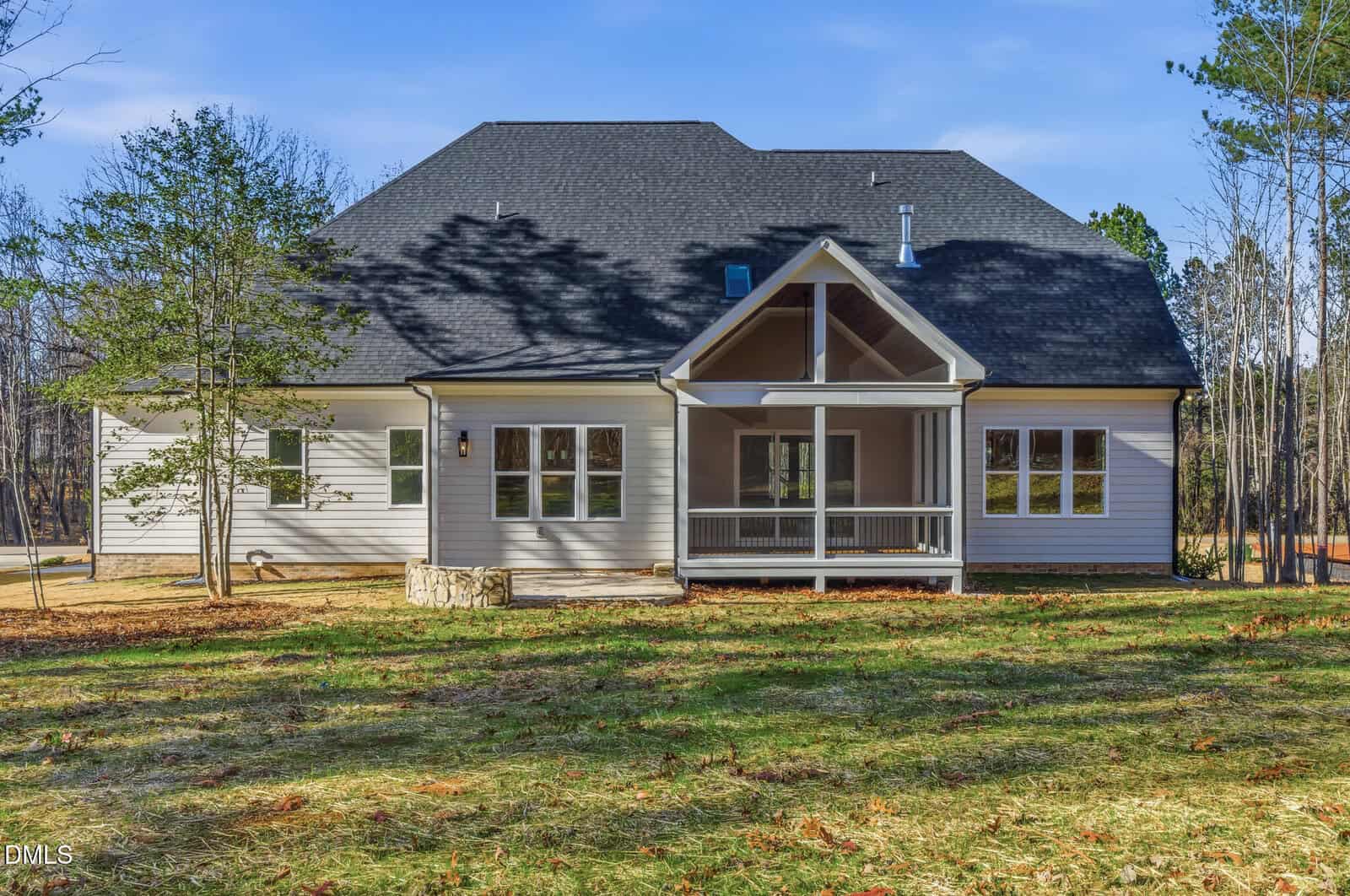 The rear exterior of a modern two-story house with light-colored siding, multiple windows, a covered porch with a gable roof, and a grassy yard bordered by trees.