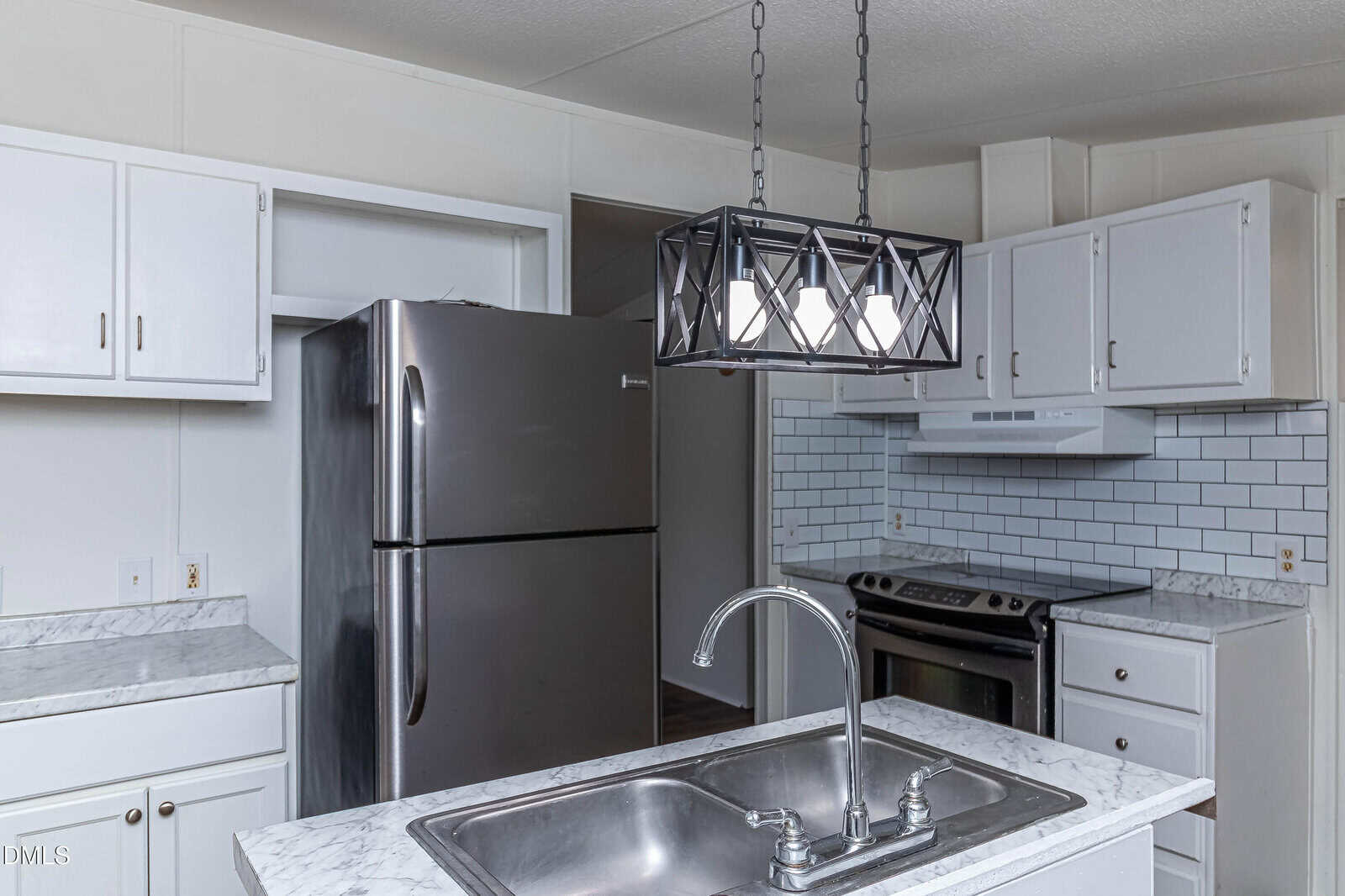 Modern kitchen with stainless steel fridge, stove, white cabinets, blue subway tile backsplash, marble countertops, and a double sink on an island under a black geometric light fixture.