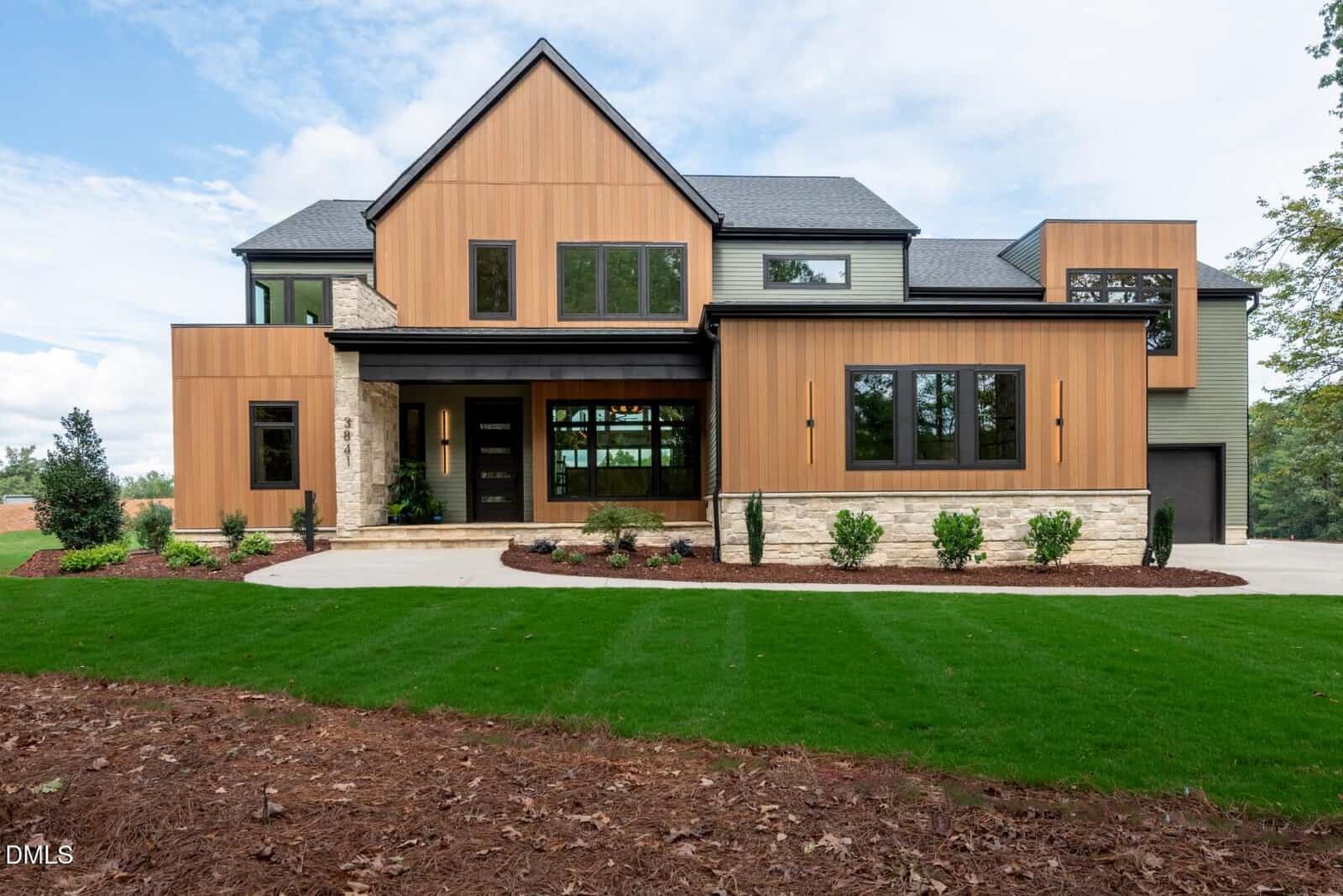 A modern two-story house at 3841 Graham Sherron Road in Wake Forest, featuring wood and stone exterior accents, large windows, a covered entryway, and a landscaped front yard with green grass and shrubbery.
