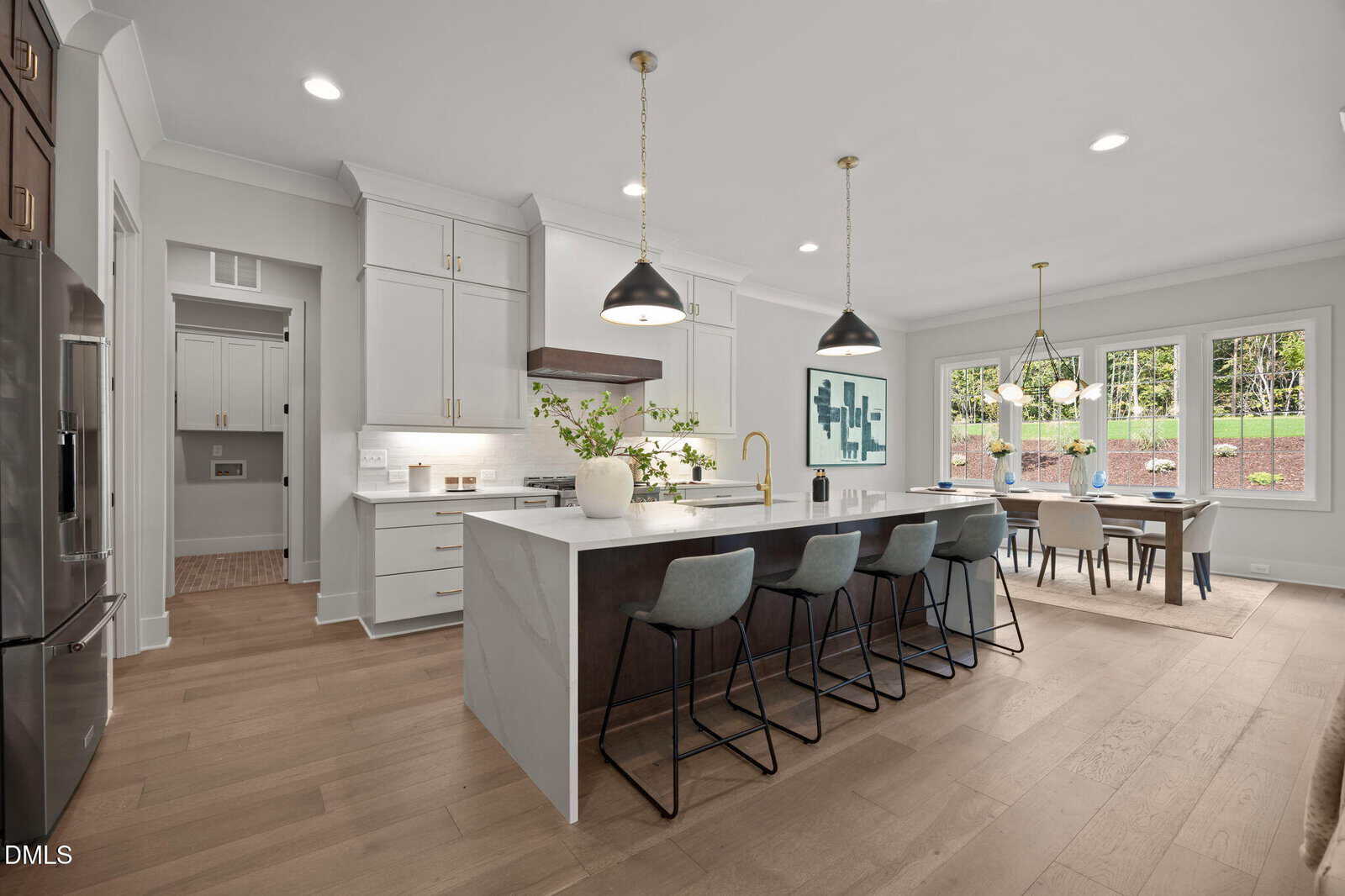 Modern kitchen with white cabinets, a large island with barstools, pendant lights, and open dining area. Big windows bring in natural light; hardwood floors and neutral decor create a spacious, inviting atmosphere.