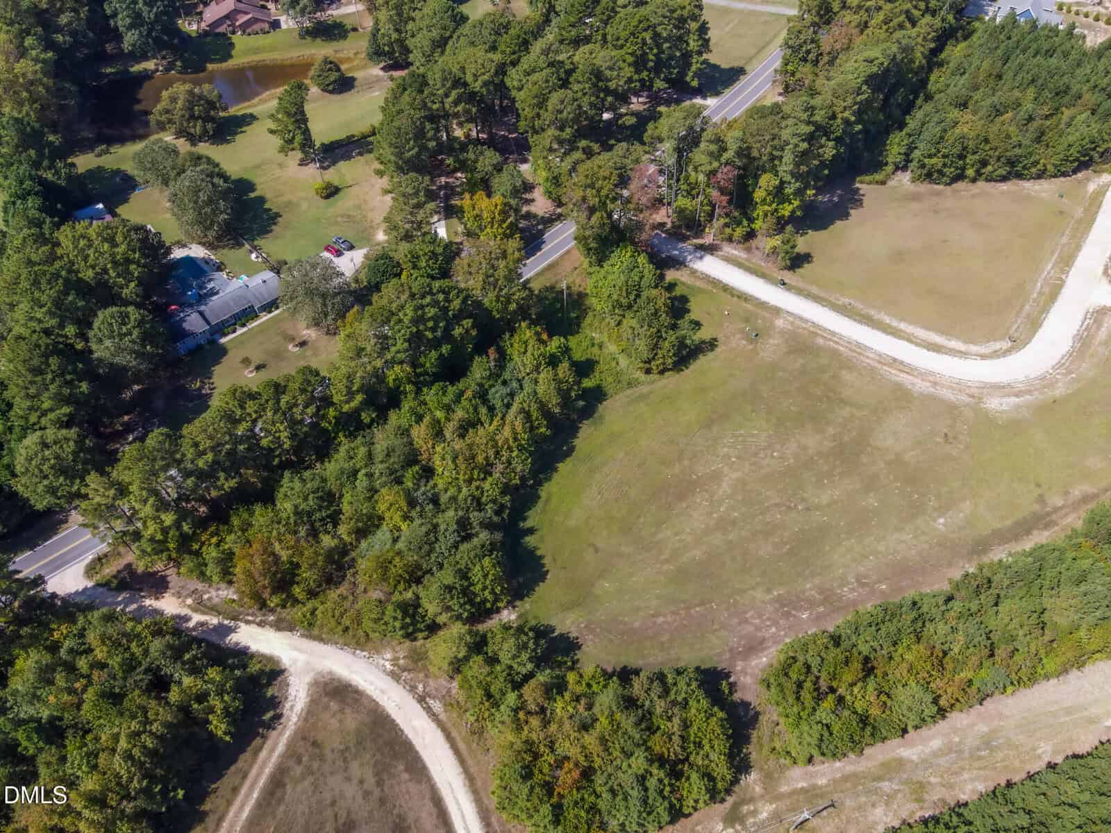 Aerial view of a rural area with winding dirt roads, grassy fields, clusters of trees, and a few houses surrounded by greenery.