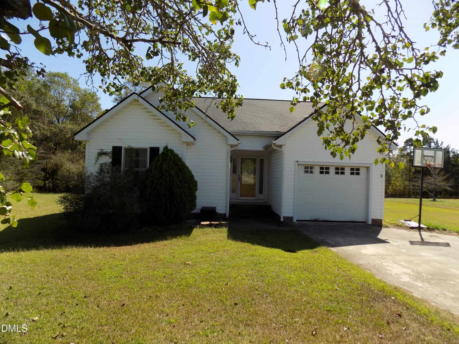 Single-story white house at 285 Bradford Ridge Drive, Youngsville, featuring a charming front porch, attached garage, and basketball hoop in the driveway. The home is surrounded by grass and trees, with shadows cast on the lawn.
