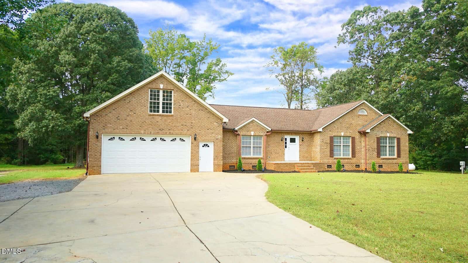 A one-story brick house at 604 S Chavis Street in Franklinton features a two-car garage and dormer window, set on a large lawn with a concrete driveway. Trees and greenery surround the property under a partly cloudy sky.