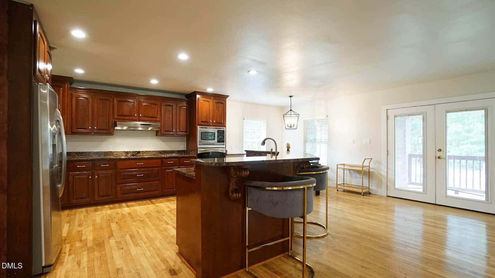 Spacious kitchen with wooden floors, dark wood cabinets, stainless steel appliances, an island with a sink, and French doors leading outside. Two chairs are placed at the island.