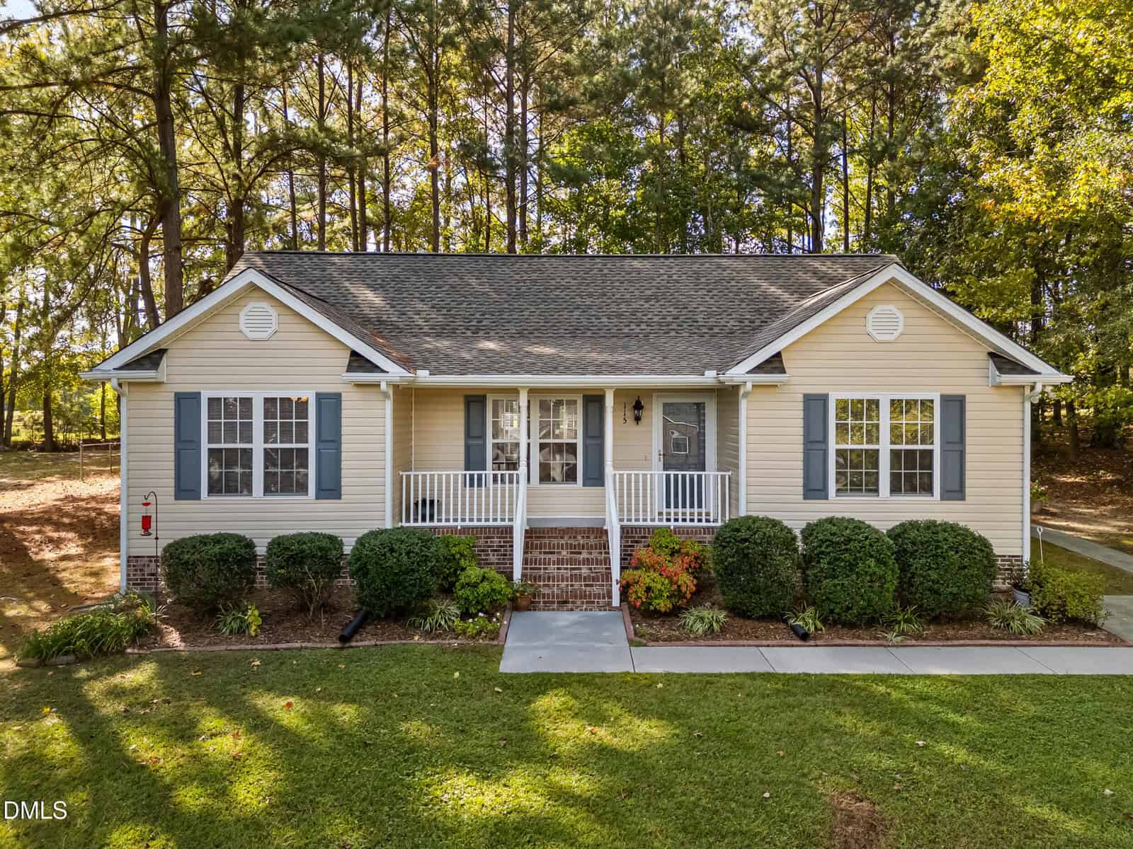 A one-story beige house with blue shutters, a front porch, white railing, and brick steps sits at 115 W Quailridge Road in Oxford. Shrubs line the front, with a sidewalk and tall trees in the background.