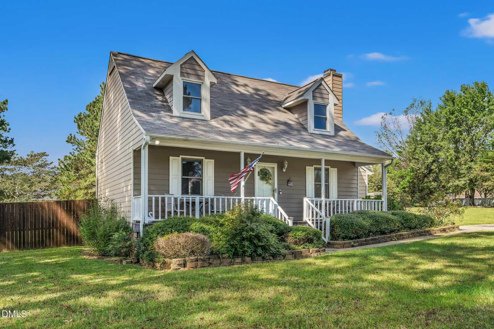 A two-story house at 62 Stoneridge Drive in Henderson features a covered front porch, dormer windows, and an American flag by the door. The landscaped yard includes bushes and grass under a clear blue sky.