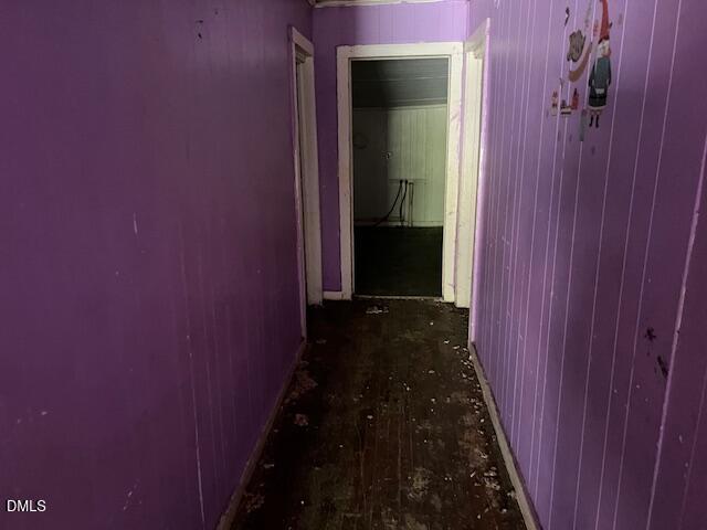 A narrow hallway with purple walls and a dark, worn wooden floor leads to two doorways. The walls show some visible wear, and there are a few small decorations on the right wall.