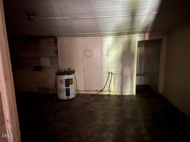 Dimly lit room with a water heater against one wall, loose wires hanging down, a tiled floor, and the shadow of a person holding a light visible on the back wall.