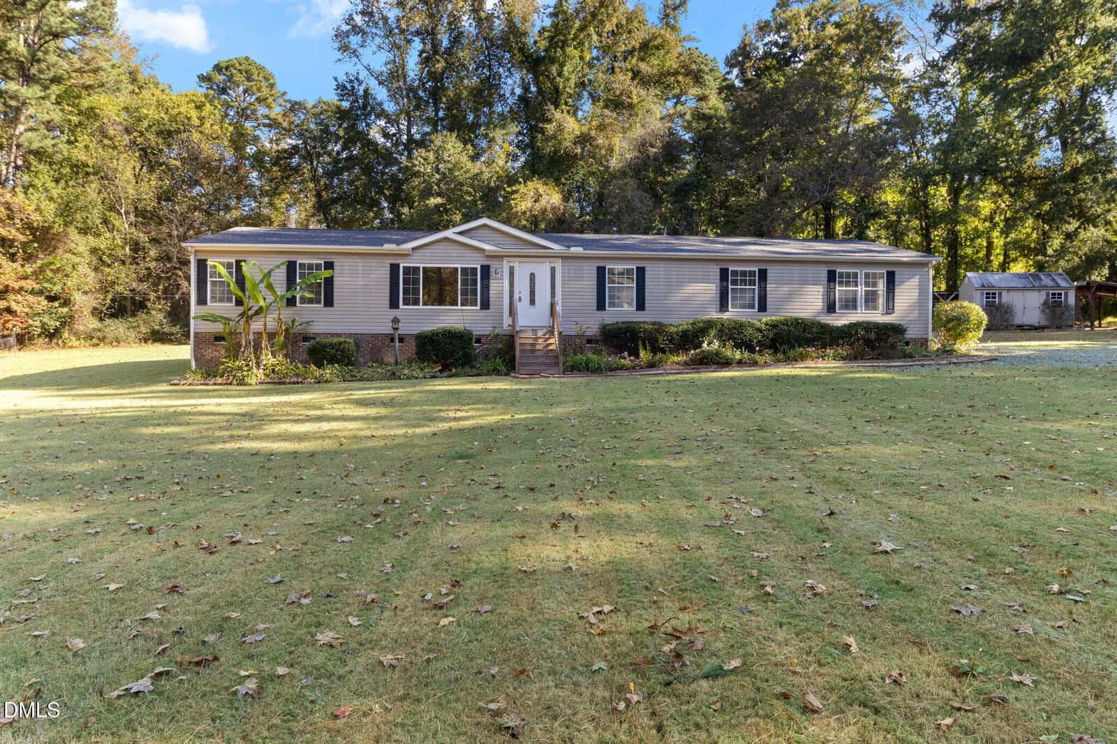 A one-story, light gray manufactured home with white trim and a front porch sits on a large, grassy lawn at 106 Lyon Street, Stem, surrounded by trees. A small shed is visible in the background to the right.