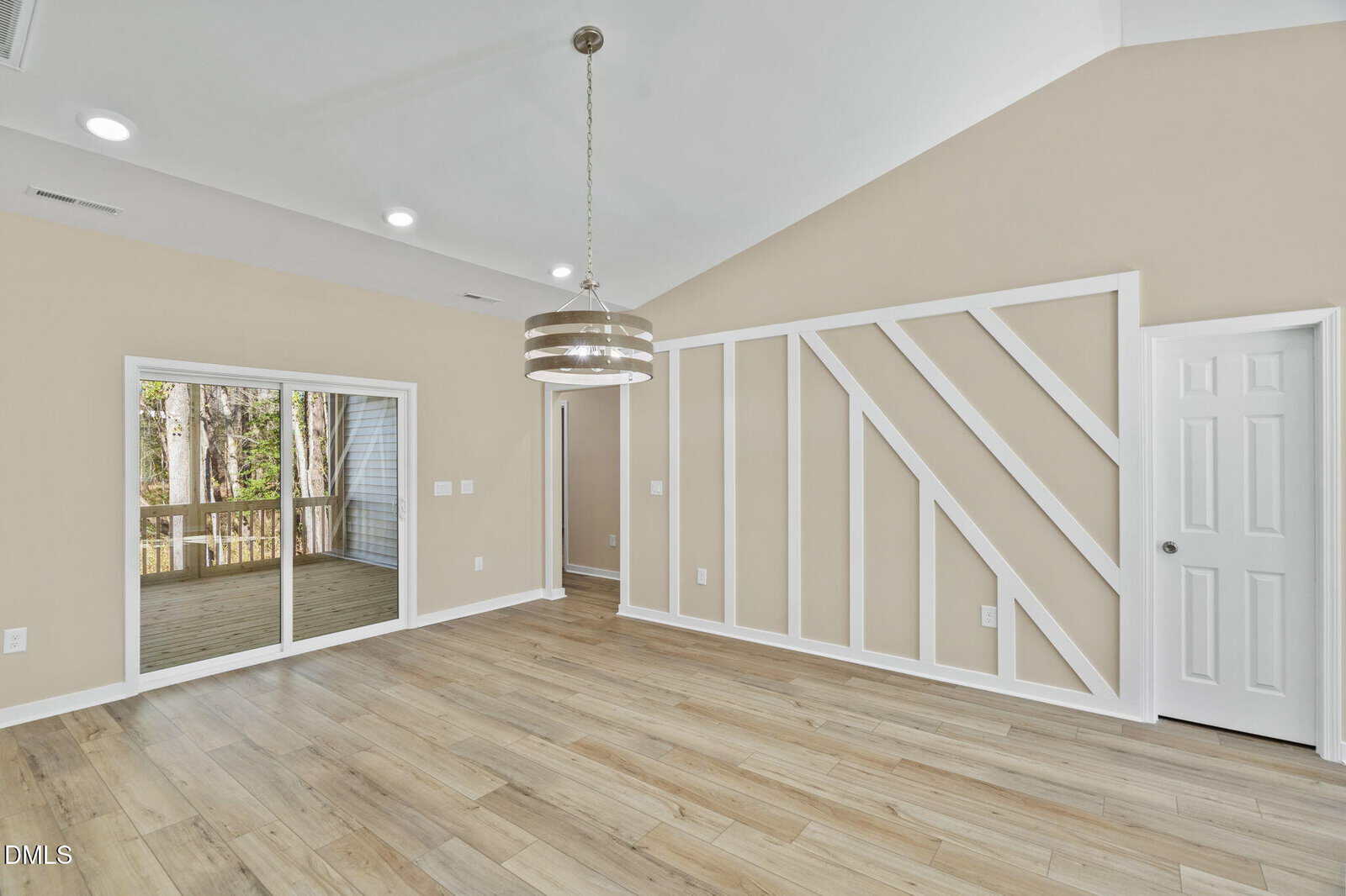 Modern empty room with light wood floors, tan walls, geometric white wall trim, a contemporary chandelier, glass sliding doors leading to a porch, and a white door on the right side.