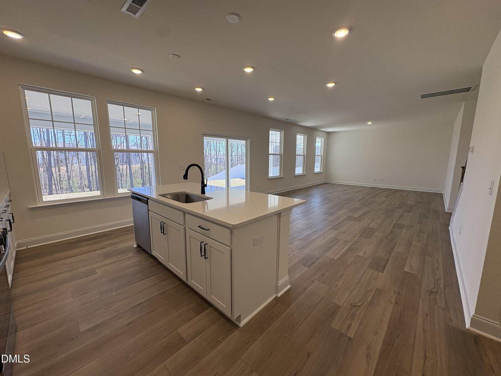 Spacious open-concept living area with large windows, wood-style flooring, and a modern kitchen island with a sink. Natural light fills the room.