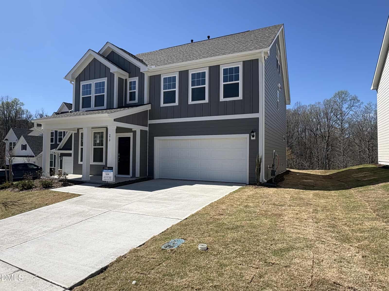 A modern two-story house with gray siding, white trim, and a covered front porch. The home features a double garage, a wide driveway, and a freshly landscaped front yard under a clear blue sky.