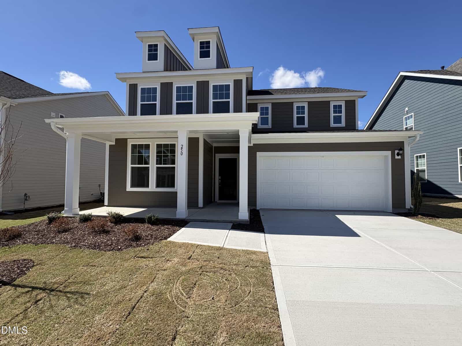 Two-story modern suburban house with a covered front porch, gray siding, white trim, double garage, and well-maintained lawn on a sunny day.