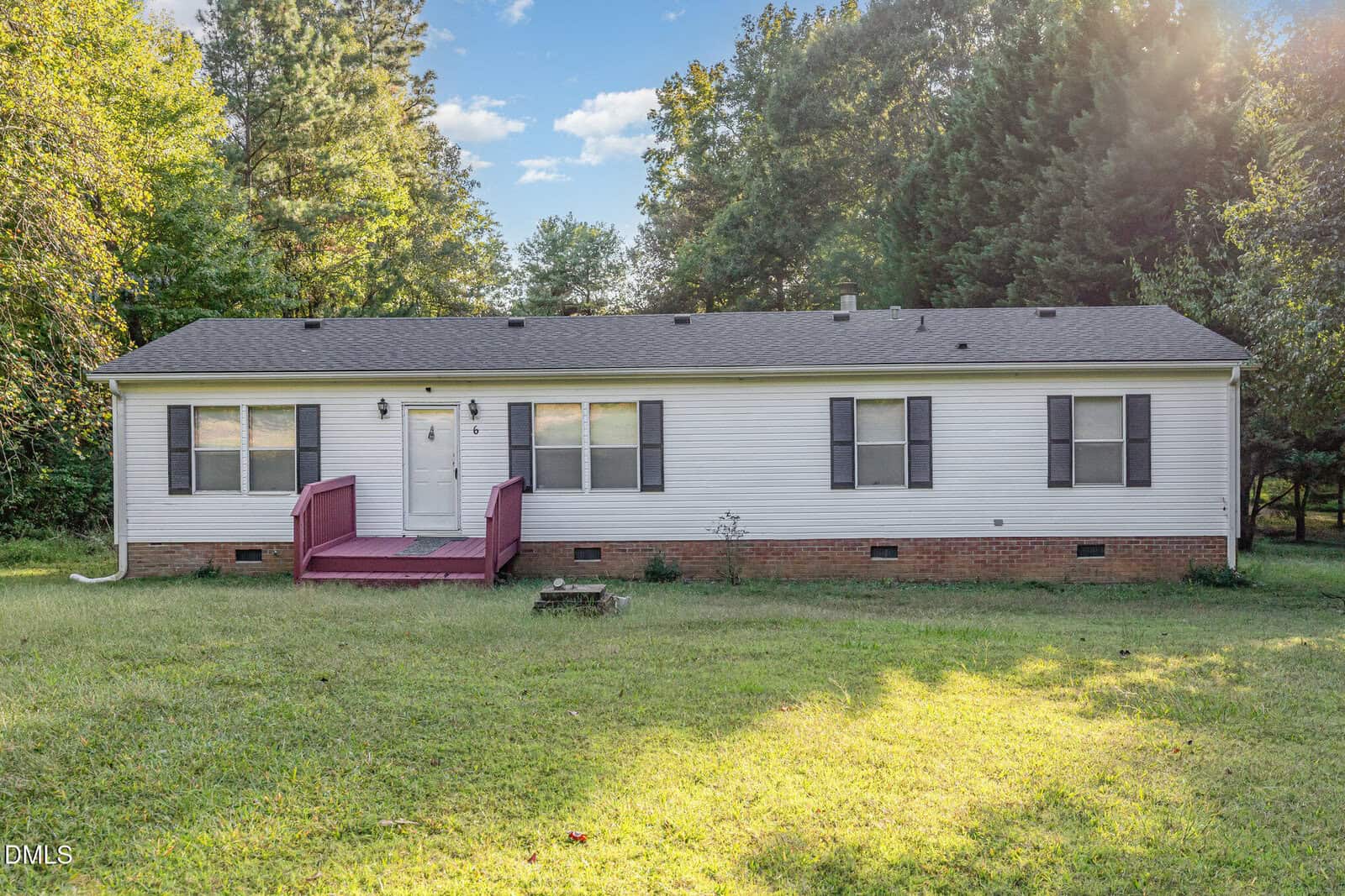 A single-story white house with a red front porch, black shutters, and a brick foundation sits on a grassy lawn surrounded by trees under a partly cloudy sky at 6 Park Avenue in Franklinton.