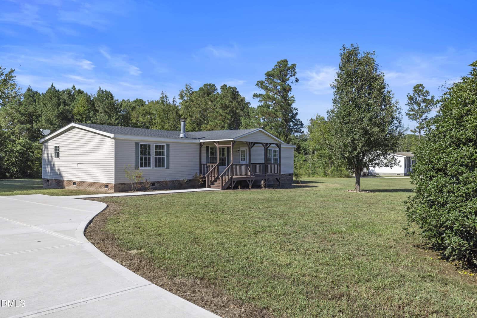 Single-story manufactured home at 276 Floyd Road in Louisburg featuring a small front porch, steps leading to the entrance, and a tree in the front yard. The house sits on a large grassy lot with a curved concrete driveway and a wooded area in the background.