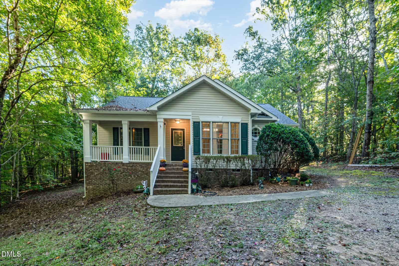 Single-story house with light siding, a covered front porch, and a dark green door surrounded by trees in Franklinton. The front yard at 55 Hardwood Drive features a curved walkway, landscaped plants, and a gravel driveway.