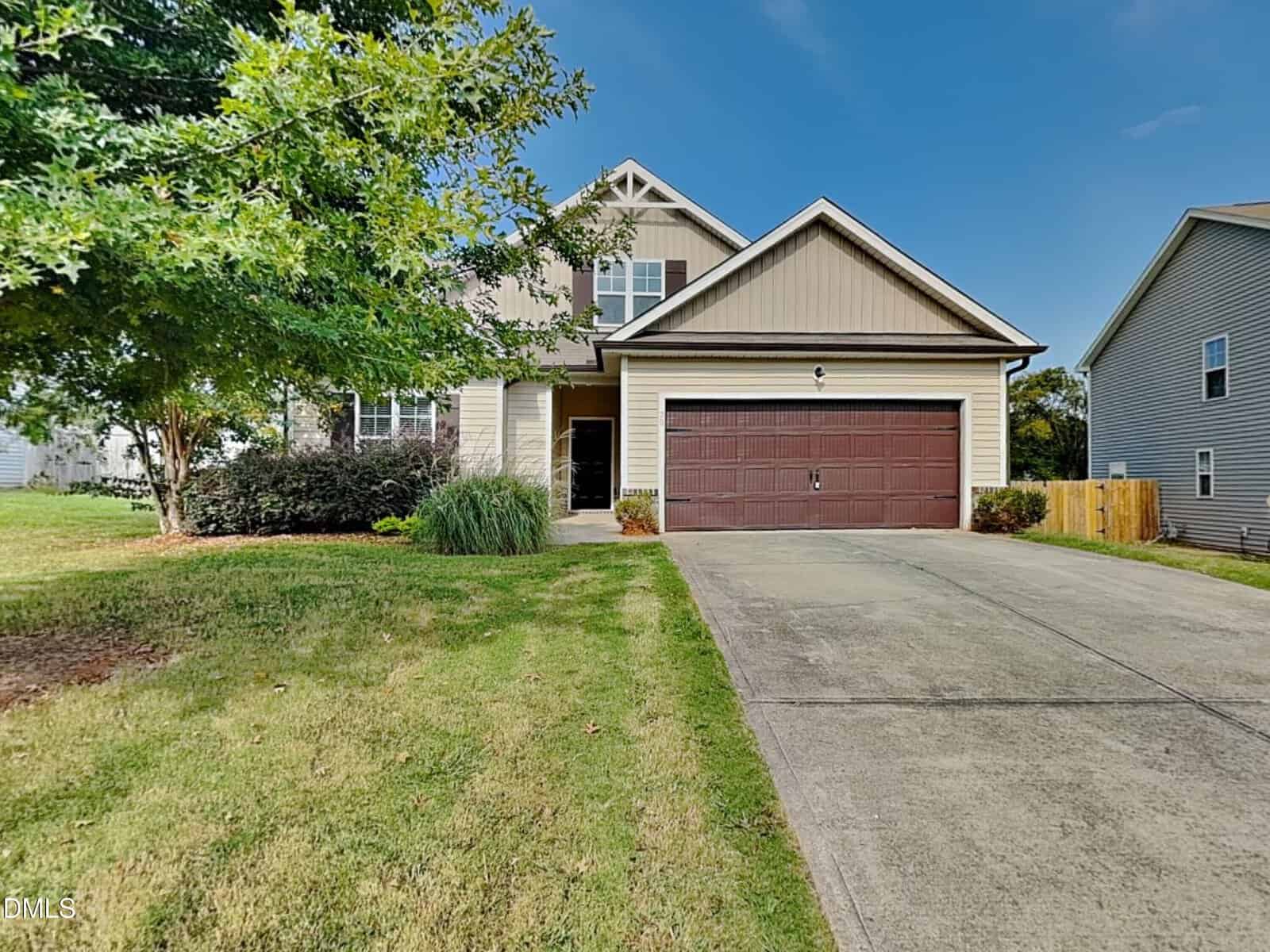 Located in Youngsville, this two-story house at 75 Ambergate Drive features beige siding with brown accents, a double garage with dark brown doors, a concrete driveway, and a well-kept front yard with green grass and a large tree on the left.