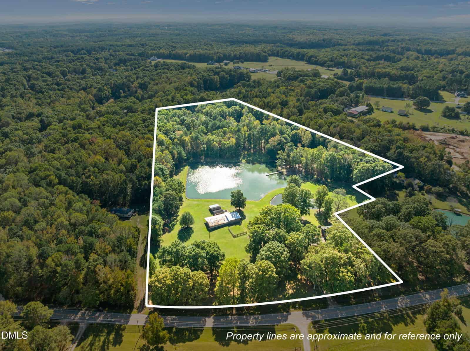 Aerial view of a wooded property at 917 John Mitchell Road, Youngsville, with a pond and several buildings outlined in white. Surrounded by forest, with roads and fields nearby. Text notes property lines are approximate.