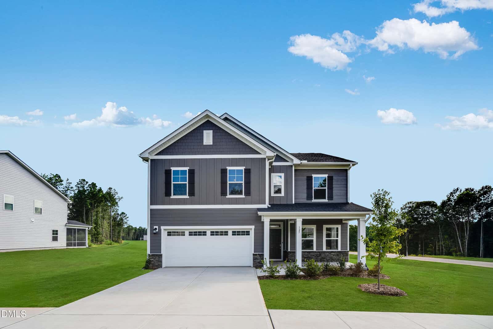 Two-story gray house with white trim, double garage, front porch, small tree, and well-kept lawn. Set on a spacious lot at 325 Sutherland Drive in Franklinton, the home features mature trees and a neighboring property visible in the background under a blue sky.