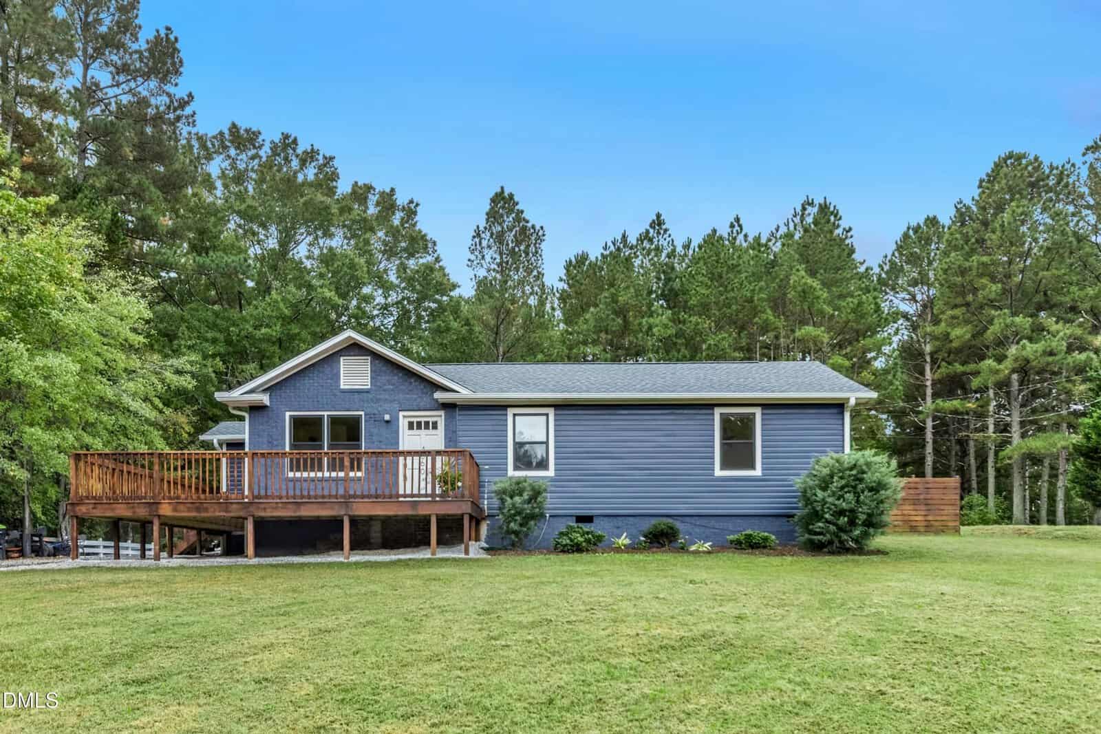 A single-story blue house with white trim sits on a grassy lawn at 4660 Dorsey Road, Oxford, featuring a wooden deck on the left side and surrounded by trees under a clear blue sky.