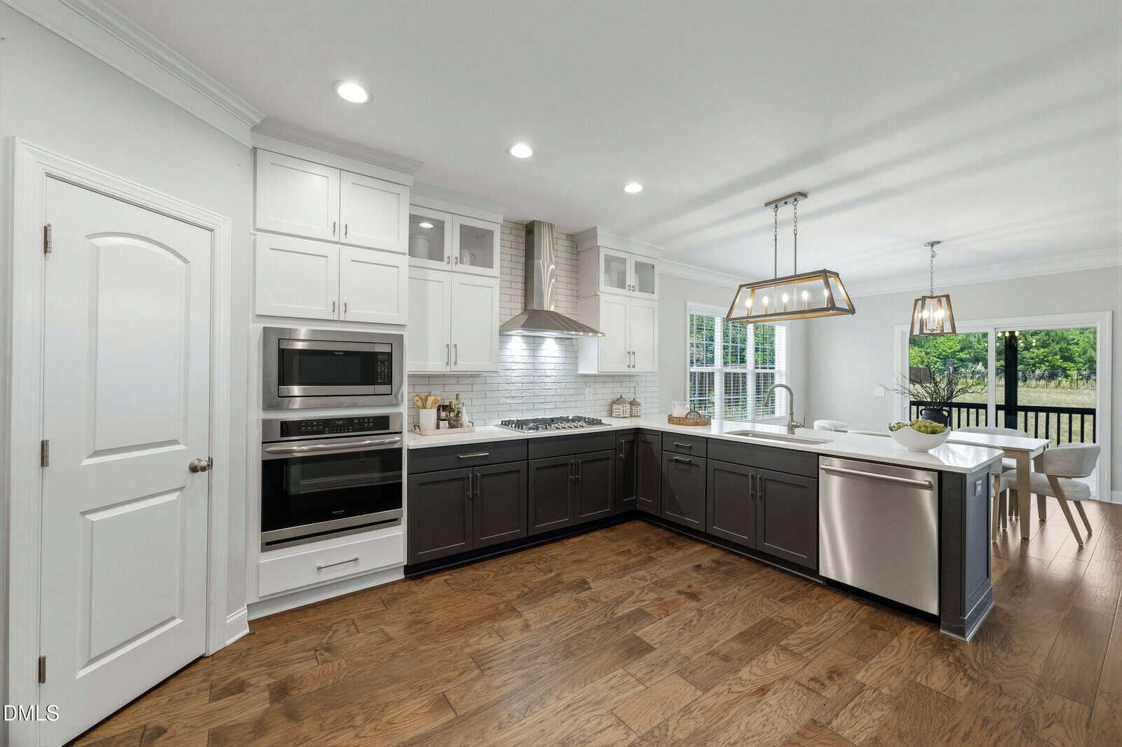 Modern kitchen with white upper and dark lower cabinets, stainless steel appliances, a tile backsplash, wood floors, and pendant lights over a peninsula. Dining area with large windows and sliding glass door to a deck.