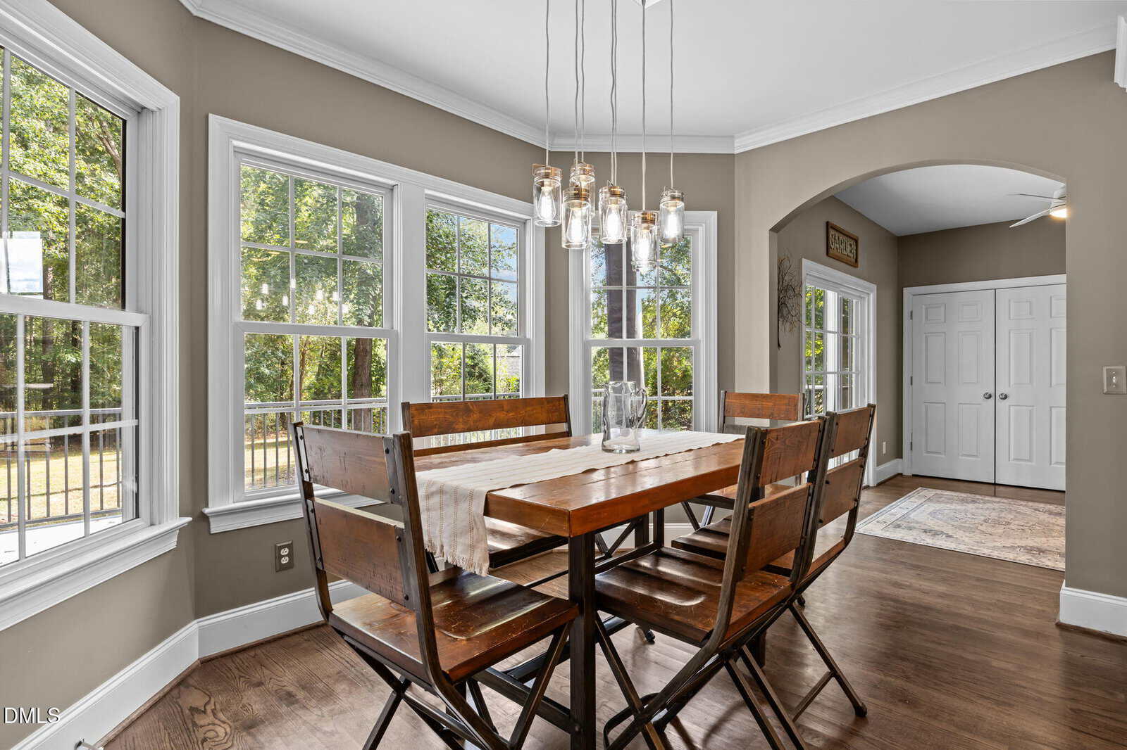 Bright dining area with a wooden table and six chairs near large windows, pendant lights above. Hardwood floors and neutral walls create a cozy, inviting atmosphere.