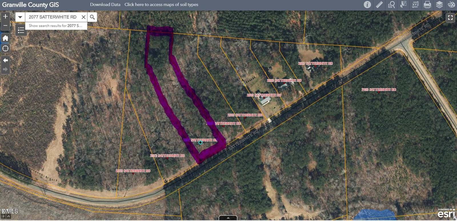 A GIS map view shows a section of wooded land with property boundary lines outlined in yellow, one plot highlighted in purple. Several labeled parcels and a few structures are visible near a curved road.