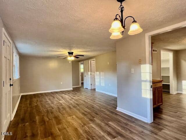 A spacious living area with light wood flooring, beige walls, a ceiling fan, and a three-light chandelier. Multiple doorways lead to other rooms, and there are built-in shelves visible in one adjoining space.