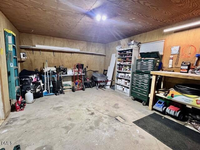 A spacious garage with unfinished wood walls and ceiling, tools and equipment neatly organized on shelves, a green tool chest, a workbench, shelving, and various items stored along the walls and floor.