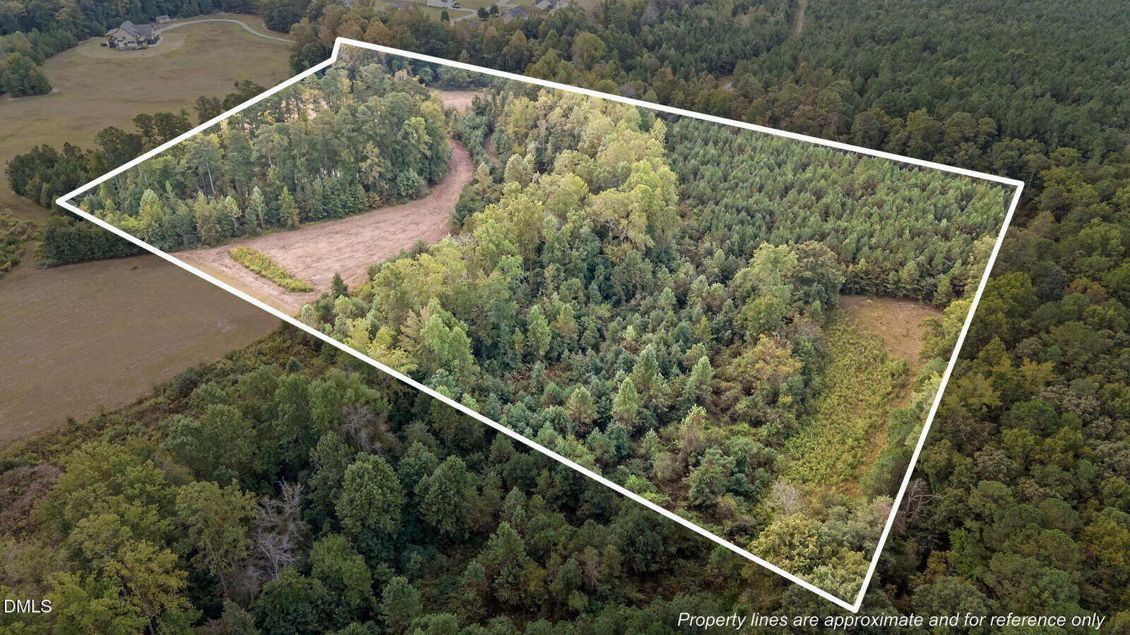 Aerial view of a wooded property with a cleared area, outlined in white to indicate approximate property boundaries. Dense trees and some open land are visible within the outlined section. Text notes property lines are approximate.