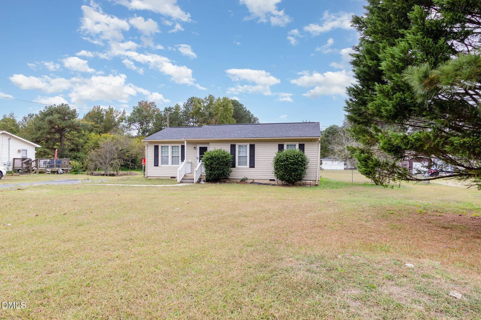 A small beige single-story house with white trim, front steps, and bushes by the entrance sits on a large grassy yard under a partly cloudy sky, surrounded by trees at 870 Abbott Road in Henderson.