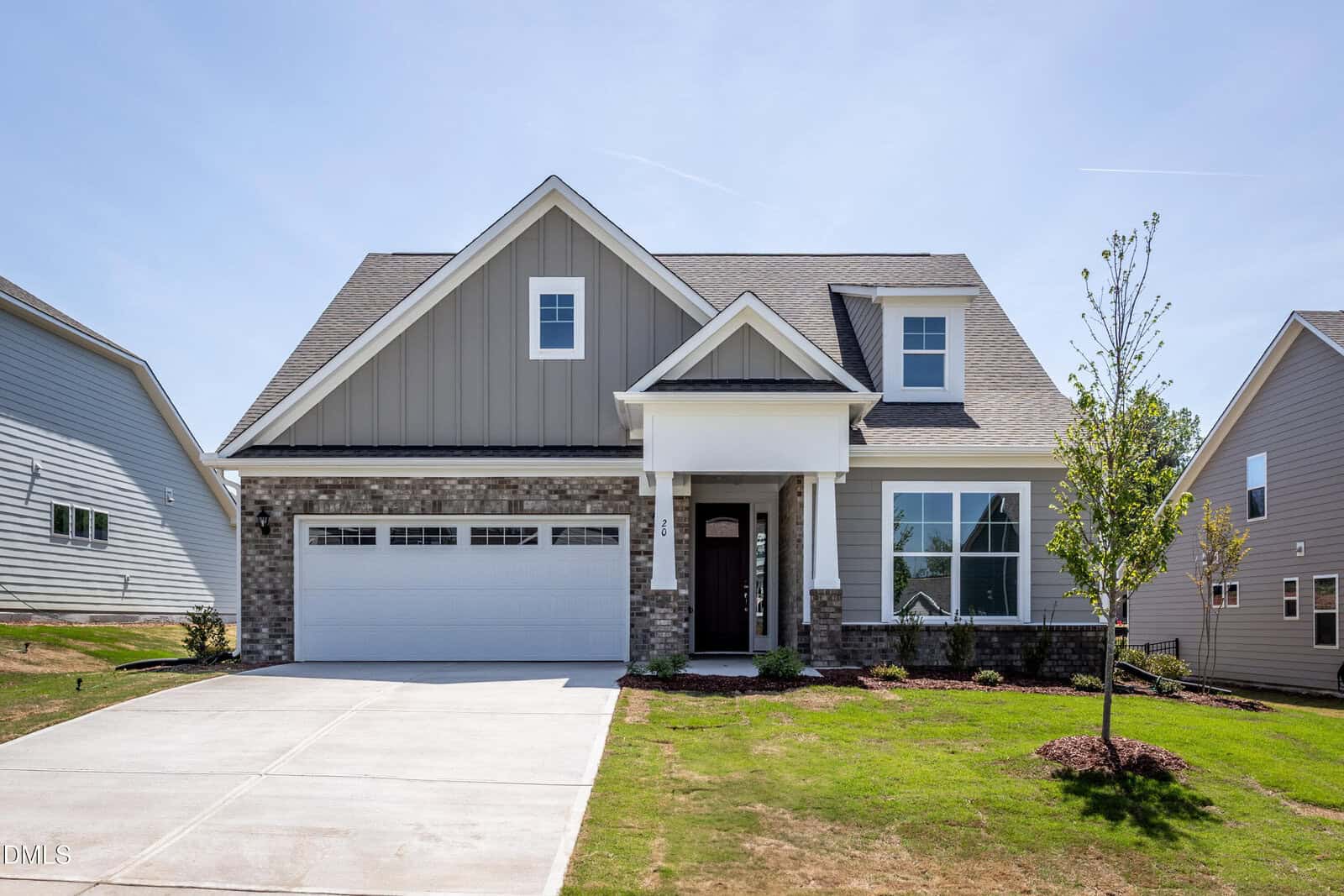 A modern two-story suburban house at 20 Slippery Elm Road, Youngsville, with gray siding, white trim, and a brick base. It features a covered front porch, two-car garage, and newly planted landscaping under a clear blue sky.