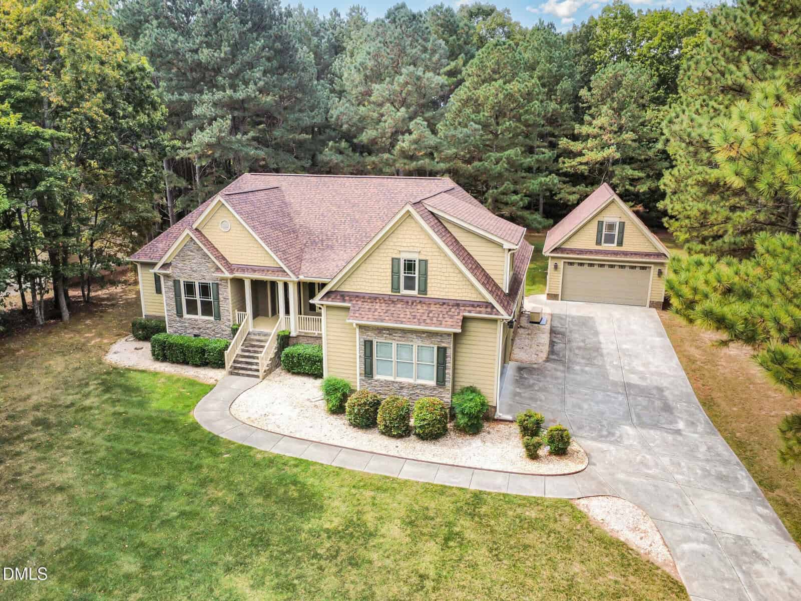 Nestled on a spacious, tree-lined lot in Youngsville, 115 Princeton Manor Drive is a beige, single-story home with gable roofs and a detached garage. A curved driveway leads past the main entrance, with trimmed bushes lining the foundation.