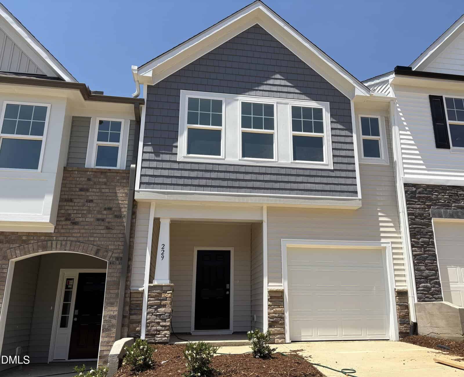 A modern two-story townhouse at 229 Alberta Drive, Franklinton, featuring gray siding, stone accents, a single-car garage, two large front windows, a black front door, and a small landscaped area with shrubs.