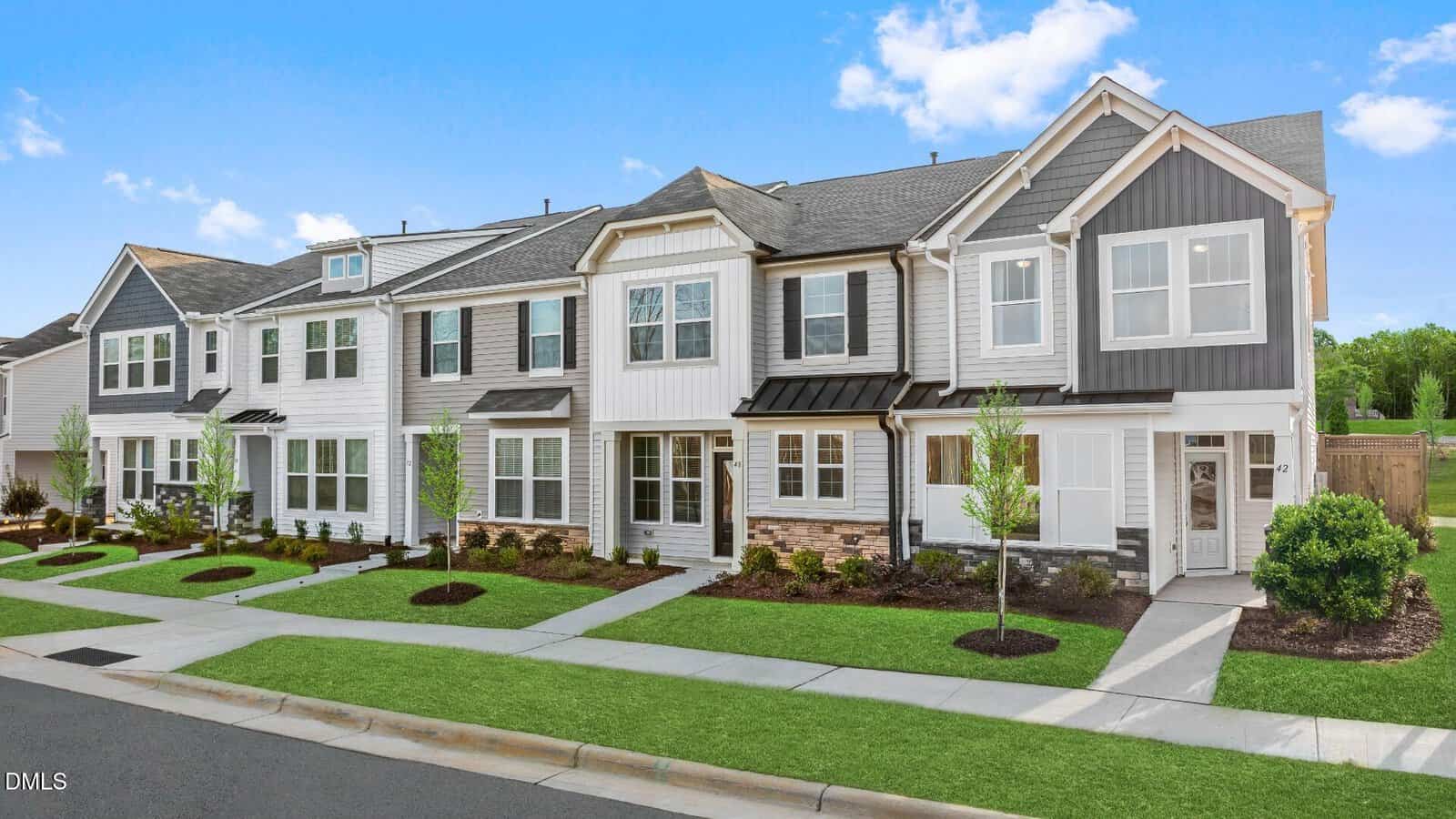 A row of modern two-story townhouses on 223 Alberta Drive in Franklinton features white and gray exteriors, landscaped front yards, young trees, and a clean sidewalk under a bright blue sky with scattered clouds.